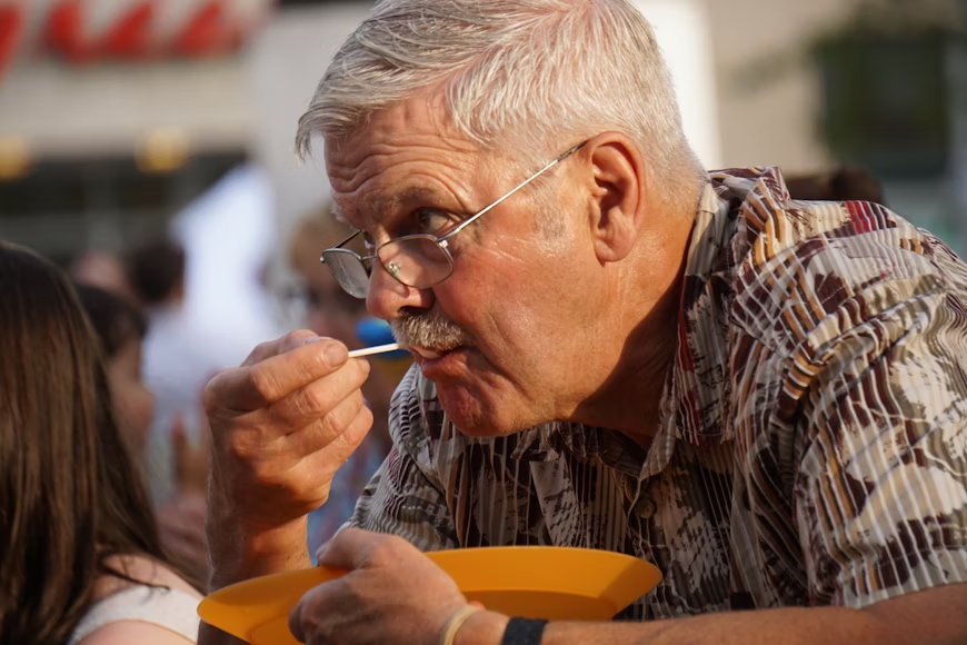Senior enjoying a healthy meal, smiling while eating fresh fruits and vegetables.