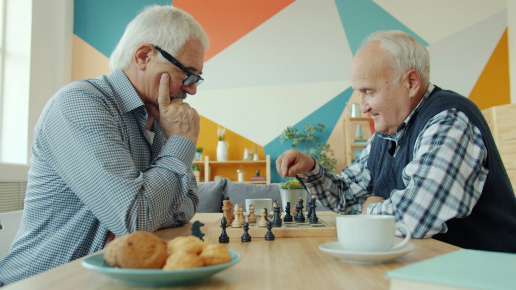 Caregiver helping a senior solve a chess game at home to reduce cognitive decline and improve memory health