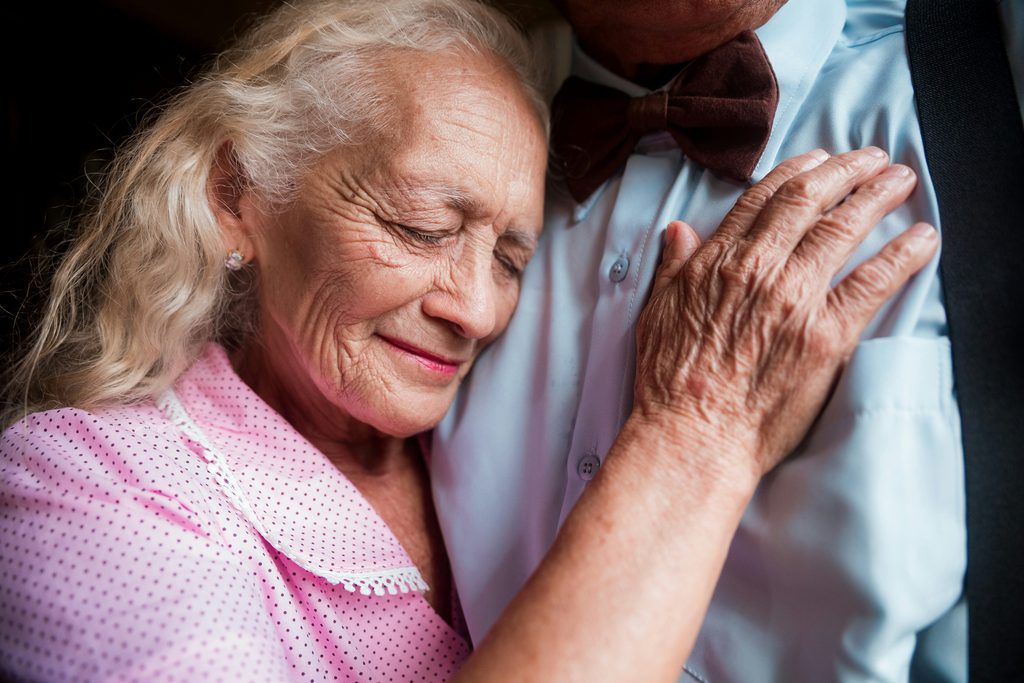 Elderly woman resting her head on her husband's chest, a moment of comfort that backup care for elderly parents helps protect